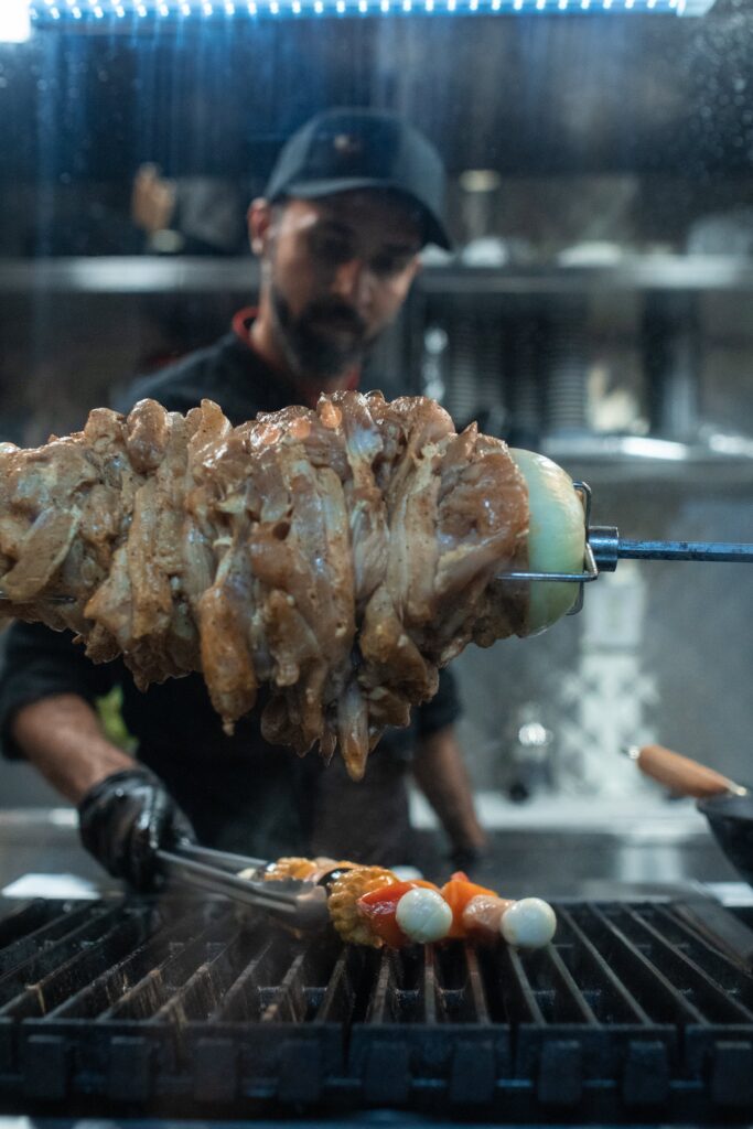 Chef grilling seasoned meat on a skewer.
