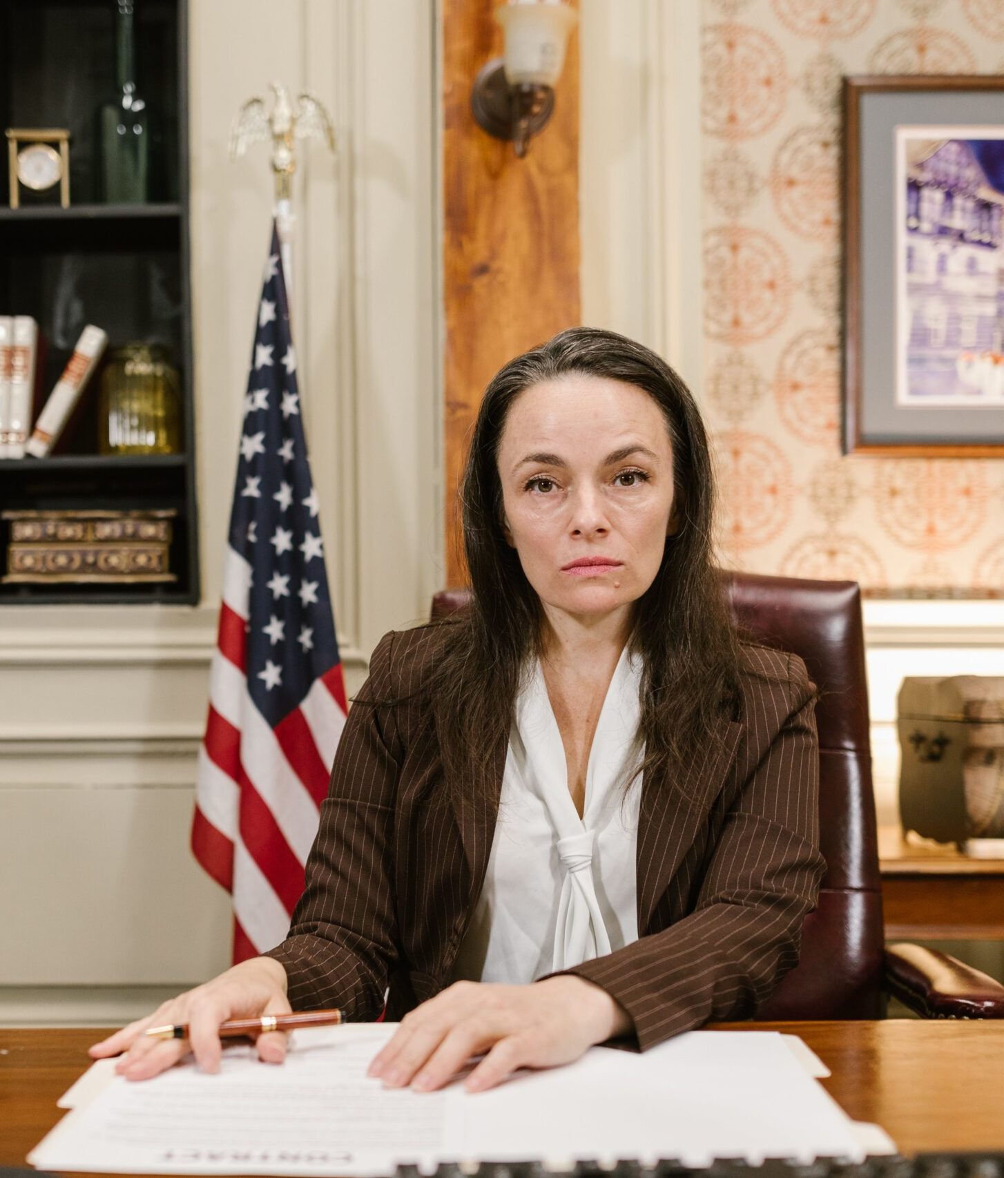 Woman sitting at a desk with an American flag behind her.