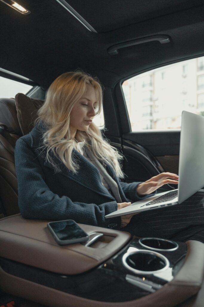 Woman working on laptop inside a car.