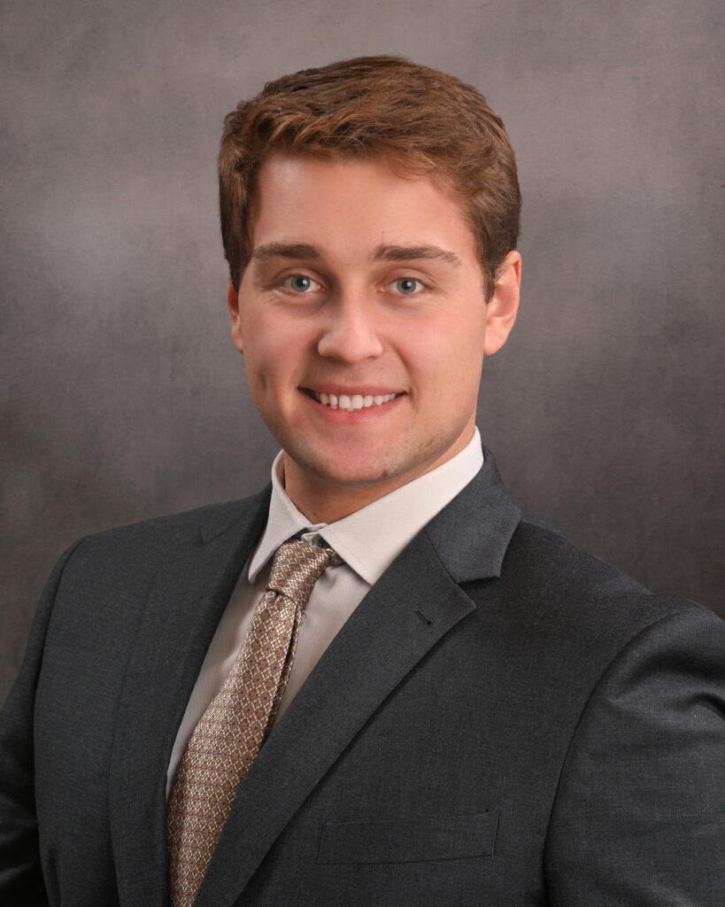 Young man in a suit smiling against a gray studio background.
